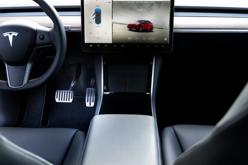 Image of inside Telsa car showing pedals showing interior, pedals, and screen.
